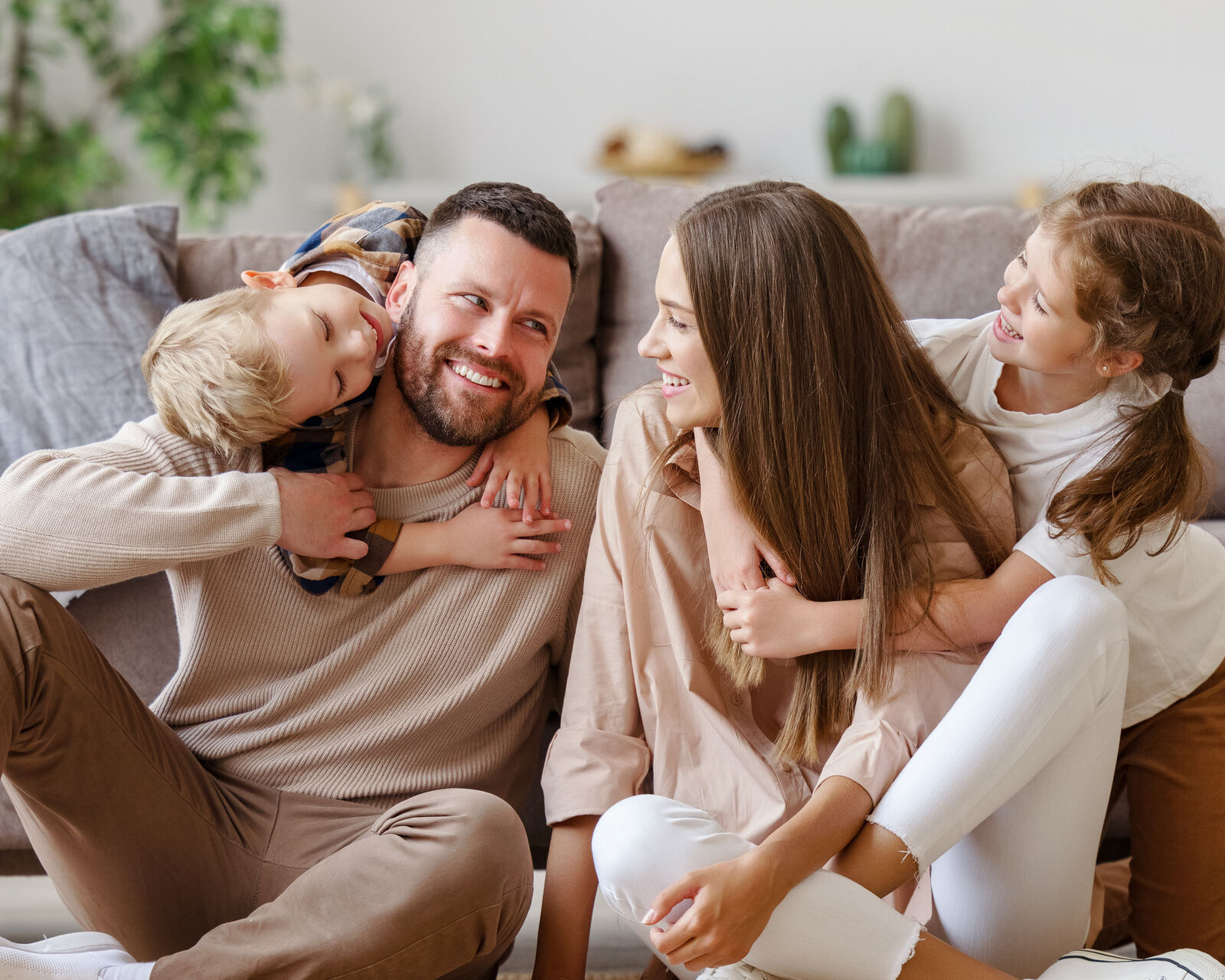 A mom and dad laughing on the living room floor with their two kids