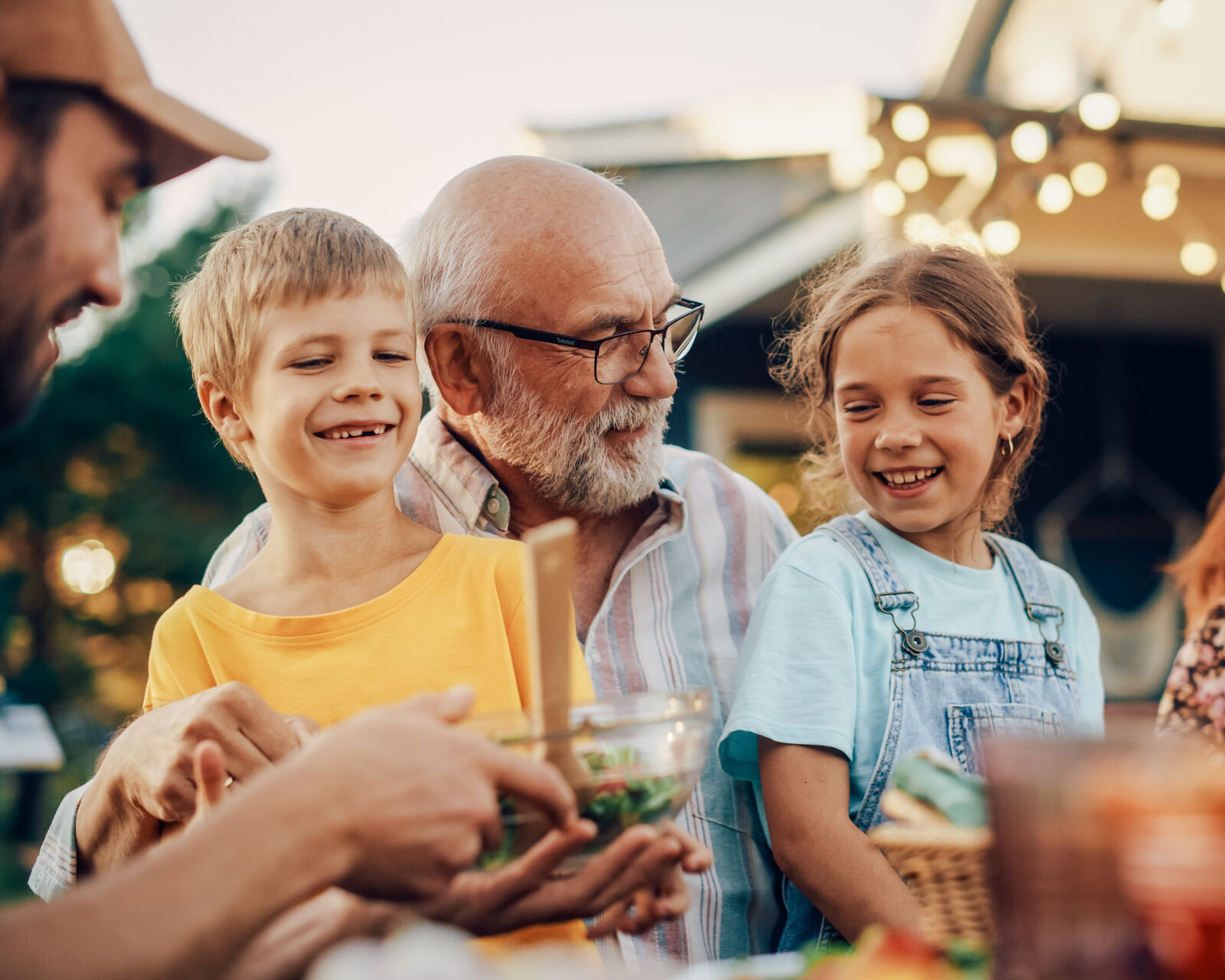 A grandfather laughing with his grandkids at an outdoor dinner