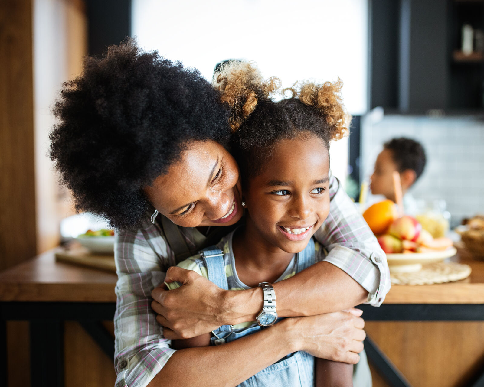 A mom hugging her laughing daughter in the kitchen