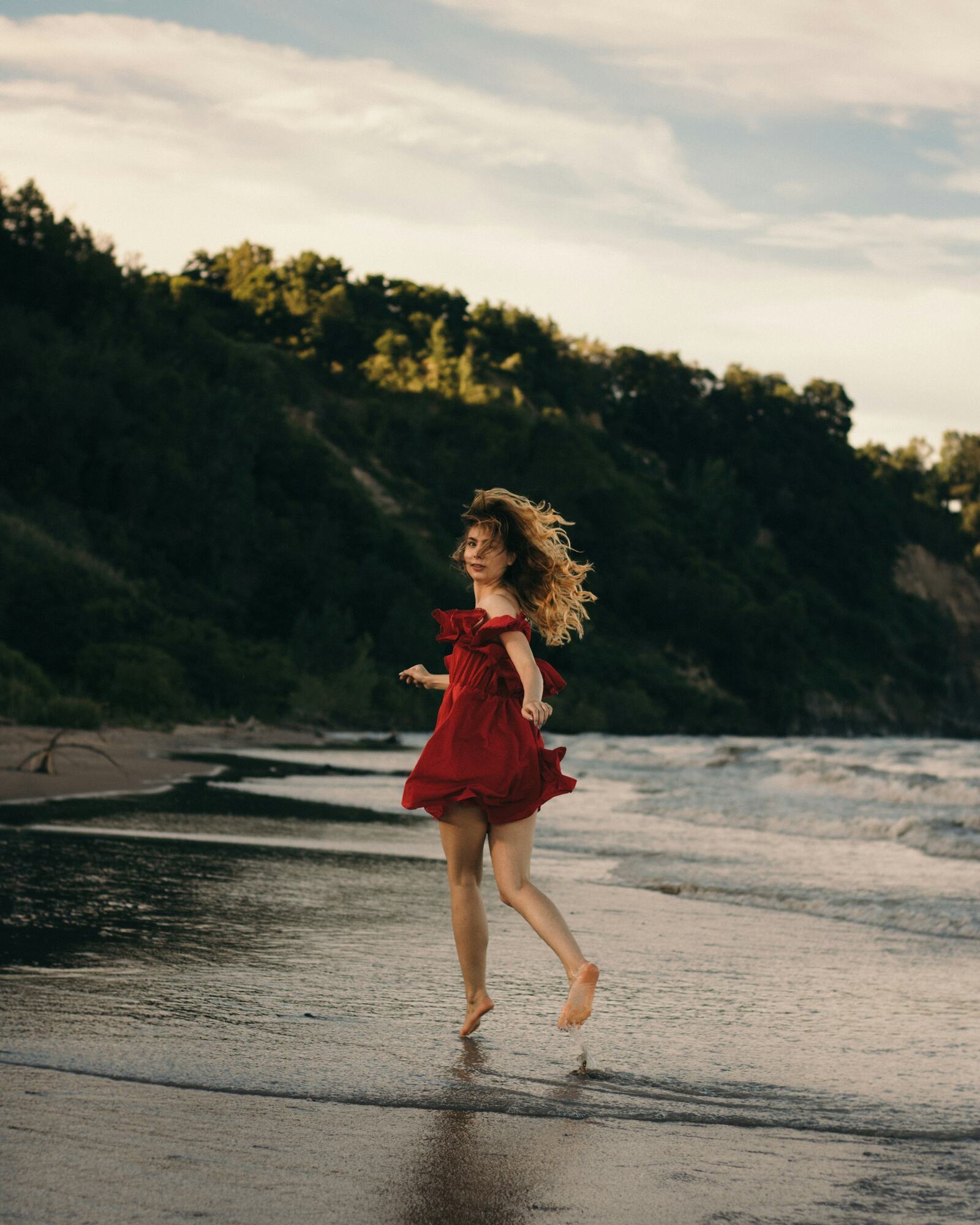 A girl in a red dress running barefoot on a beach at golden hour
