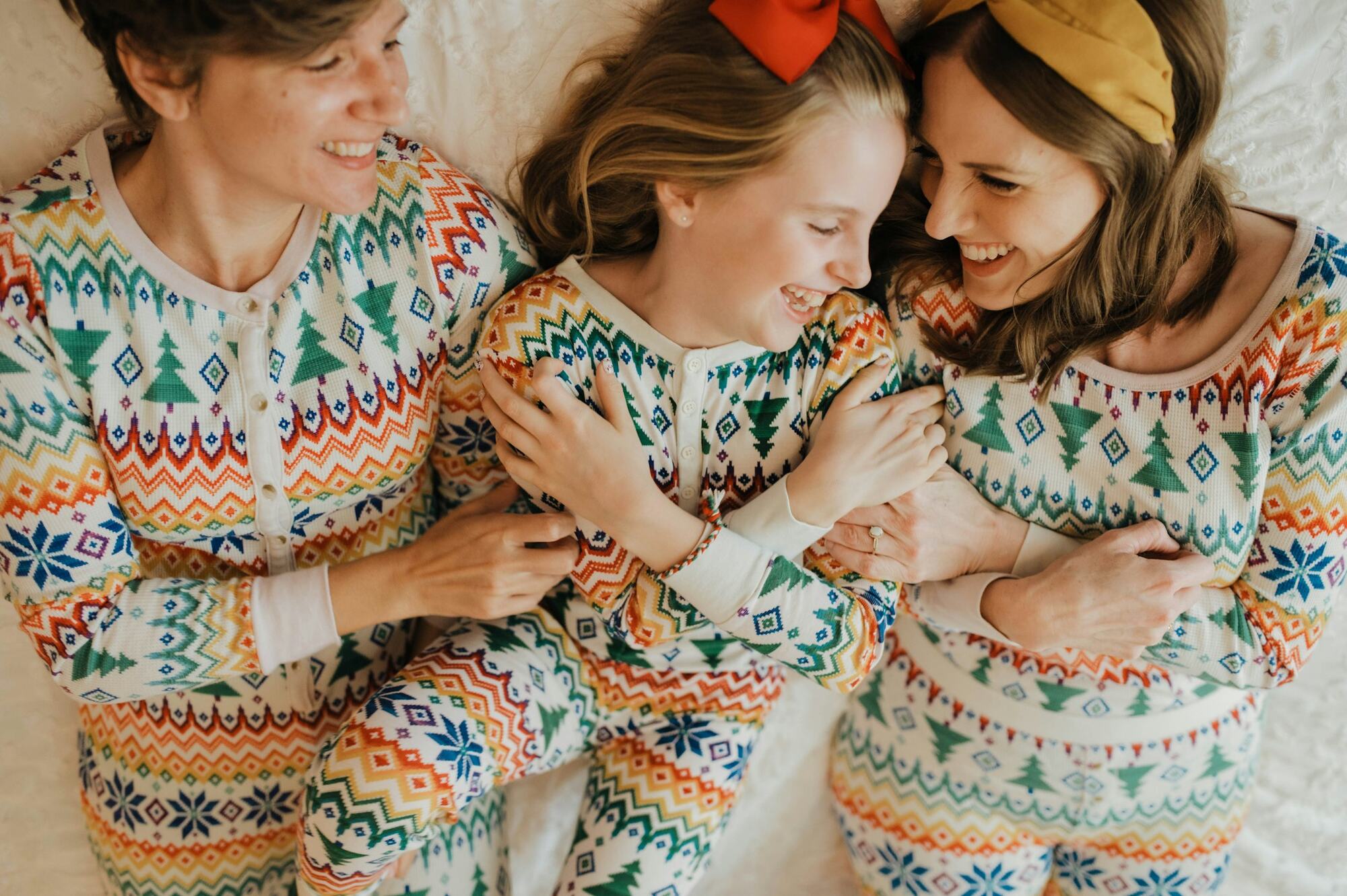 A mom and her two daughters in matching holiday pajamas, laughing