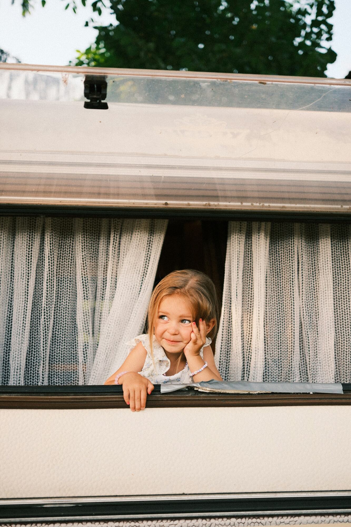 A little girl smiling out of a camper window