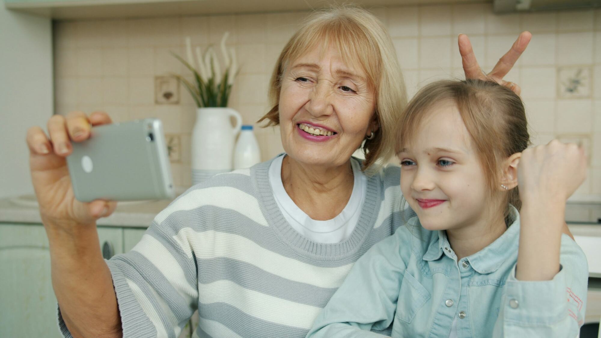 A grandmother and her granddaughter taking a selfie in the kitchen