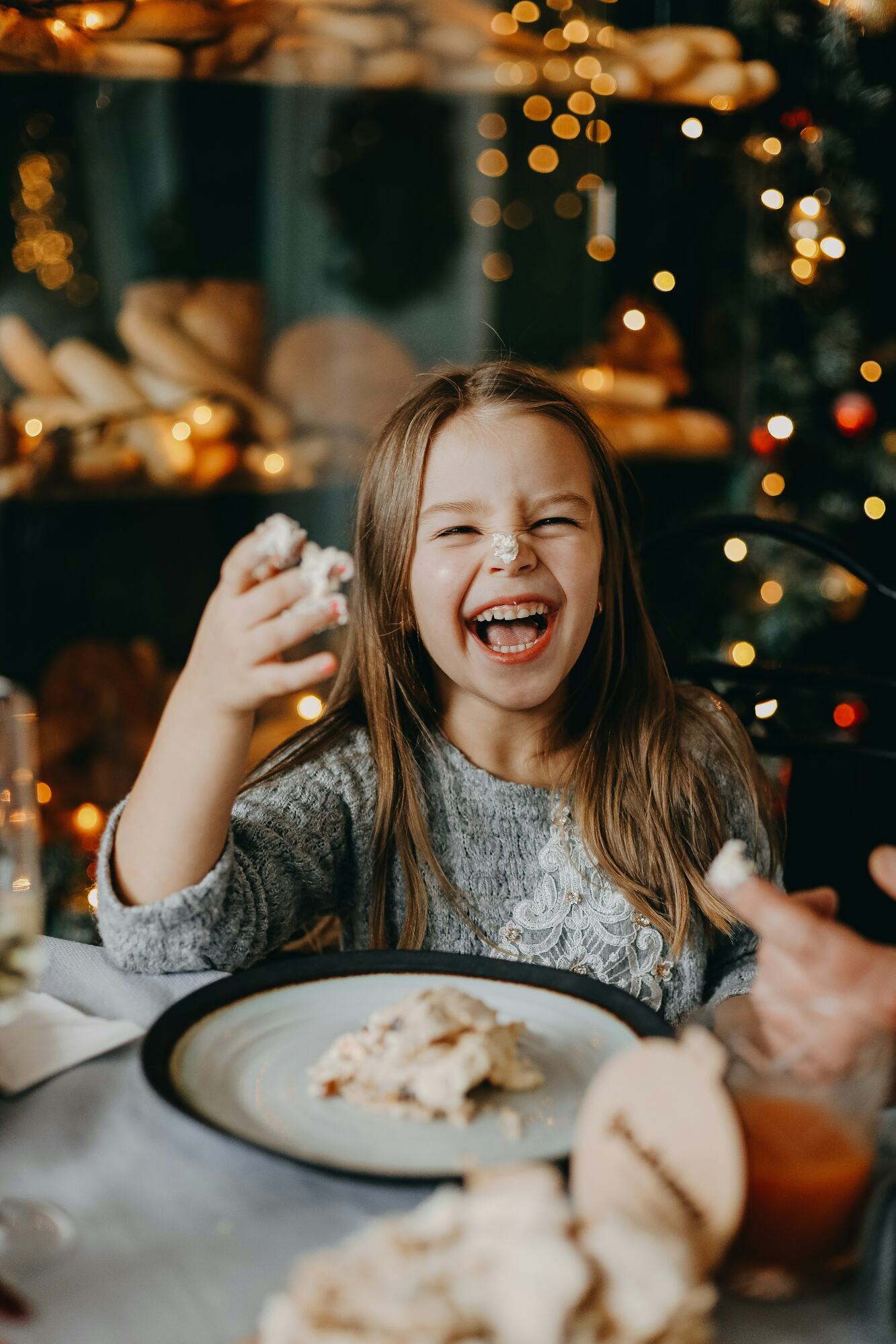 A girl laughing at a holiday table with powdered sugar on her nose