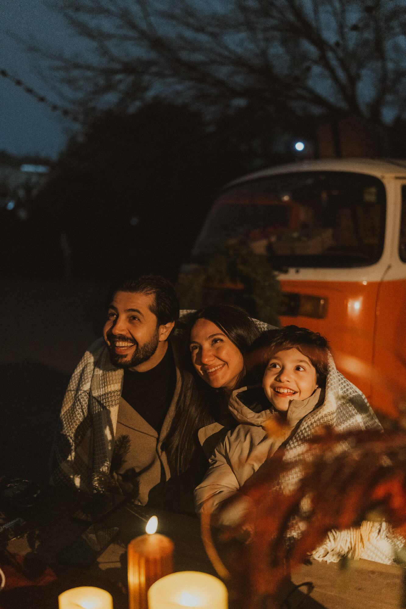 A family wrapped in blankets laughing outside a camper van at night